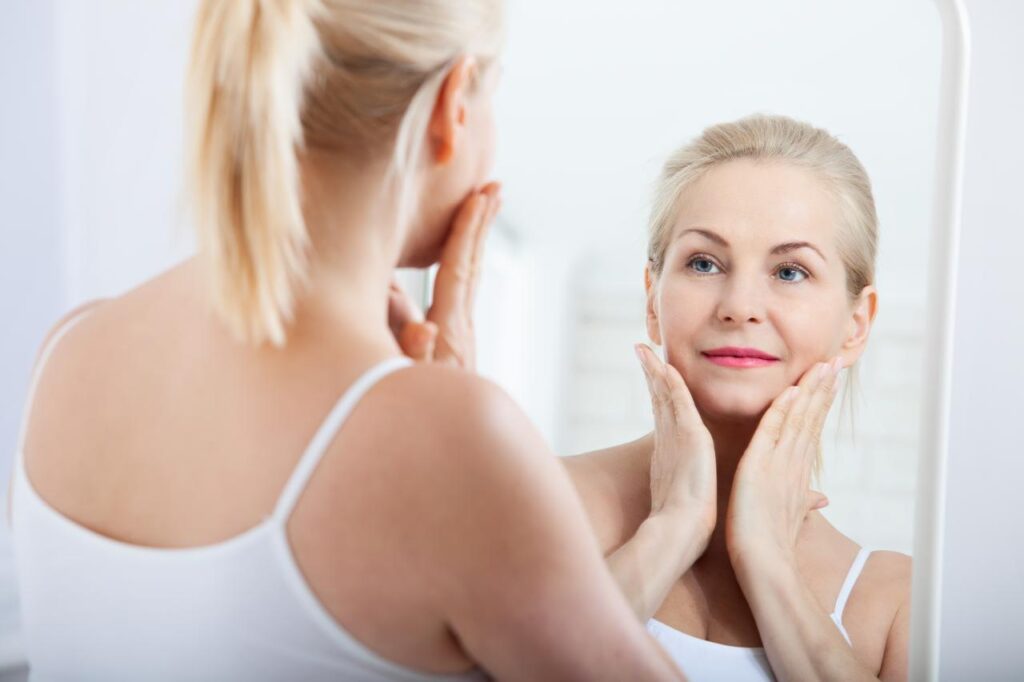 Mujer de edad avanzada viendo su rostro en el espejo después de un lifting facial